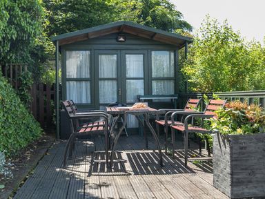 An outdoor seating area with chairs and a table on a wooden deck in front of a garden shed at 2 Rockmount in Salcombe