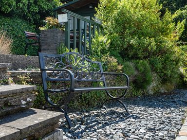 A metal garden bench on a gravel path near stone steps and green bushes at 2 Rockmount in Salcombe