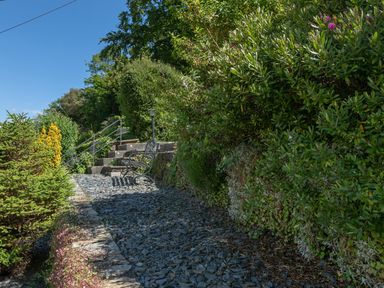 A garden path with slate stones a metal bench stone steps and green bushes at 2 Rockmount in Salcombe