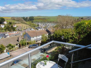 A balcony with a white table and chair overlooking a residential area with houses hills and a marina at 2 Rockmount in Salcombe