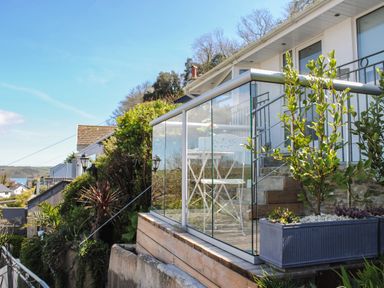 A balcony with glass railing and white chairs and table next to plants at 2 Rockmount in Salcombe
