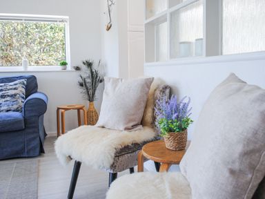 A sitting area with two chairs with cushions and sheepskin throws and a small wooden table with a potted plant next to a blue sofa at 2 Rockmount in Salcombe