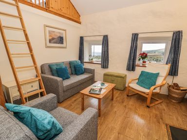 A living room with grey sofas and blue cushions a wooden coffee table and a white armchair at Y Bwthyn Elidir Fach Mountain near Llanberis