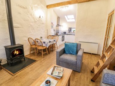 A living room with a wood burning stove a dining table with chairs and a kitchen area at Y Bwthyn Elidir Fach Mountain near Llanberis