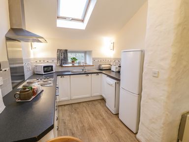 A kitchen with white cabinets a refrigerator dishwasher microwave and skylight at Y Bwthyn in Elidir Fach Mountain near Llanberis