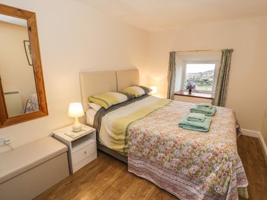 A bedroom with a double bed with floral and striped bedding two bedside tables with lamps a mirror on the wall a window with curtains and a small vase of flowers on the sill at Y Bwthyn Elidir Fach Mountain near Llanberis
