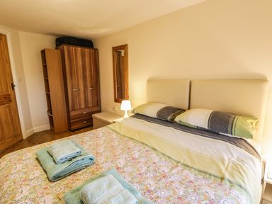 A bedroom with a double bed and folded towels on the bed a wardrobe and a lamp on a bedside table at Y Bwthyn Elidir Fach Mountain near Llanberis
