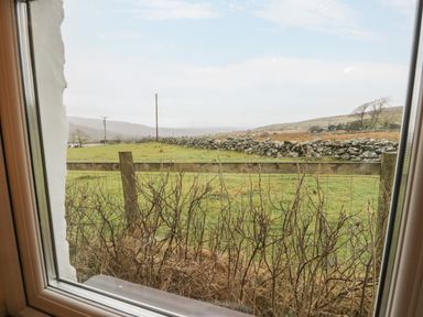 A view of countryside with grassy fields stone wall and wooden fence from a window at Y Bwthyn Elidir Fach Mountain near Llanberis