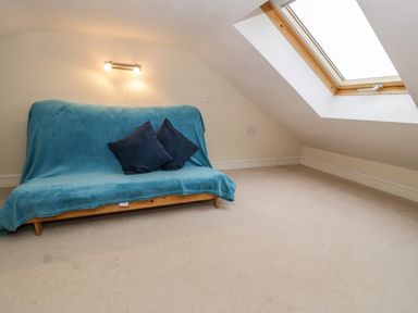 A small room with a wooden futon covered by a blue throw and two dark cushions under a wall light and a slanted skylight window at Y Bwthyn in Elidir Fach Mountain near Llanberis