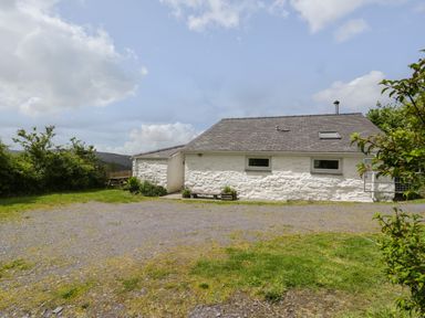 A white stone cottage with a gray roof and small windows surrounded by grass and bushes at Y Bwthyn Elidir Fach Mountain near Llanberis