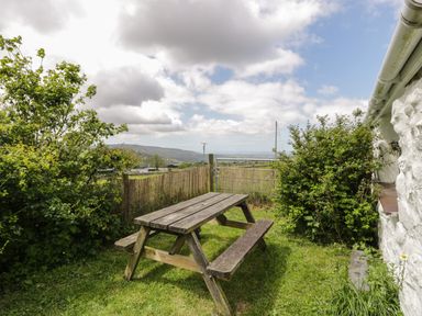 A wooden picnic table on grass next to bushes and a white stone wall at Y Bwthyn in Elidir Fach Mountain near Llanberis