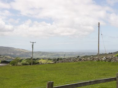 A grassy field with wooden fence posts and power lines and stone walls with hills and trees in the background at Y Bwthyn in Elidir Fach Mountain near Llanberis