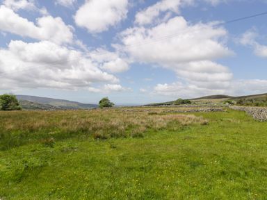 A grassy field with stone walls and hills in the background at Y Bwthyn in Elidir Fach Mountain near Llanberis