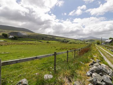 A rural landscape with a wire and wood fence alongside a dirt road and grassy fields at Y Bwthyn Elidir Fach Mountain near Llanberis