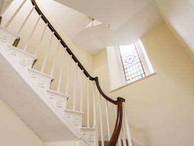 A staircase with white balusters and a dark wooden handrail near a window with stained glass at 3 Dartview in Dartmouth