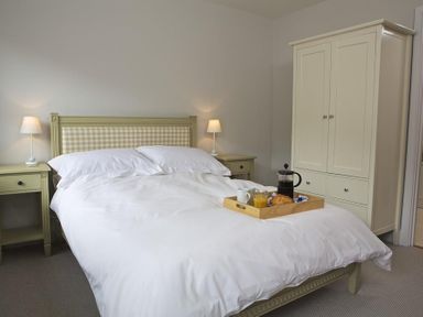 A bedroom with a bed with white bedding two bedside tables with lamps and a wardrobe with a breakfast tray on the bed at 3 Eddystone Row in Salcombe