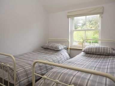 A bedroom with two single beds with plaid bedding under a window at 3 Eddystone Row in Salcombe