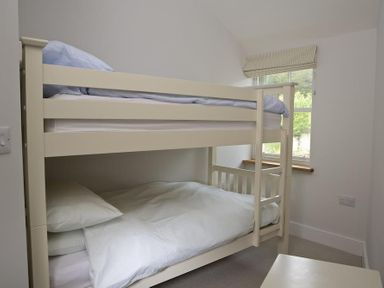 A small bedroom with cream bunk beds and a window with a blind at 3 Eddystone Row in Salcombe