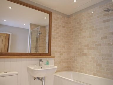 A bathroom with a sink a bathtub with shower and a large mirror at 3 Eddystone Row Salcombe