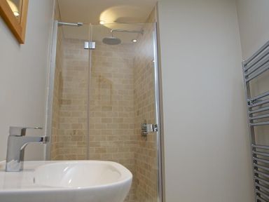 A bathroom with a sink, a glass shower enclosure with tiled walls, and a metal towel rack at 3 Eddystone Row in Salcombe