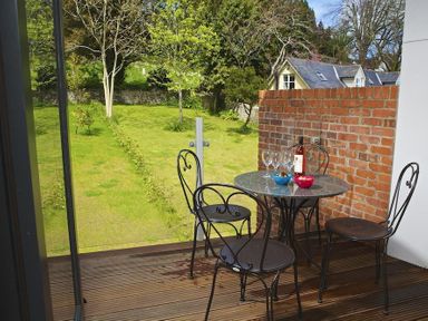 A balcony with metal chairs and a table with wine and bowls overlooking a garden at 3 Eddystone Row Salcombe