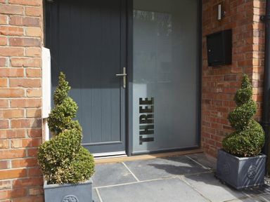 A front door with frosted glass panel displaying the word three and two spiral-shaped plants in pots at 3 Eddystone Row in Salcombe