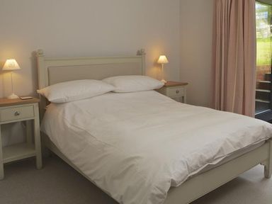 A bedroom with a double bed between two nightstands with lamps and a window with curtains at 3 Eddystone Row in Salcombe