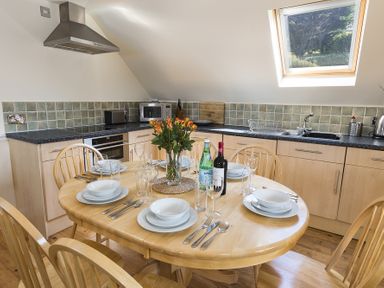 A kitchen with a round wooden dining table set for six under a skylight at 4 Armada House in Hope Cove