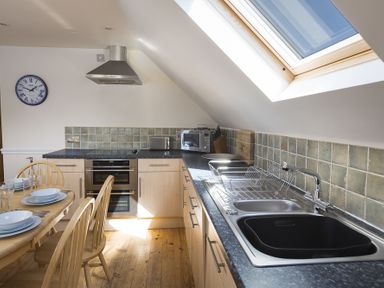 A kitchen with wooden dining table and chairs a stove sink and skylight window at 4 Armada House in Hope Cove