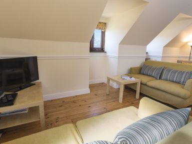 A living room with two sofas a wooden coffee table a TV on a side table and windows under sloped ceilings at 4 Armada House in Hope Cove