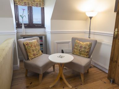 A corner seating area with two armchairs and a small round table under a window with a flower vase at 4 Armada House Hope Cove