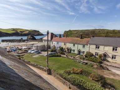 A coastal village with pastel-colored cottages near a small harbor with boats and green hills at 4 Armada House in Hope Cove