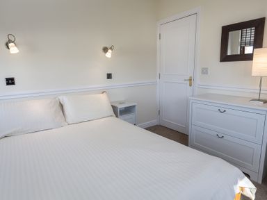 A bedroom with a white bed two wall lamps a white nightstand a white dresser with a lamp and a mirror on the wall at 4 Armada House in Hope Cove