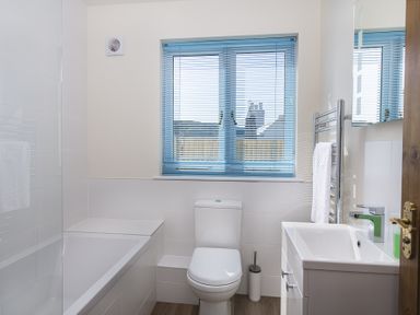 A bathroom with a bathtub toilet sink mirror and window with blue blinds at 4 Armada House in Hope Cove