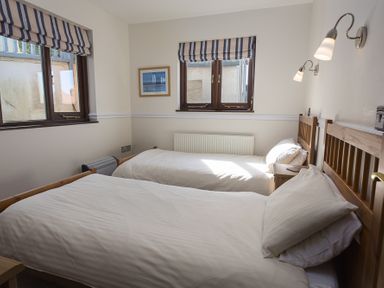A bedroom with two single beds with white bedding two windows with striped blinds and wall lamps at 4 Armada House in Hope Cove