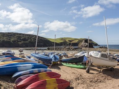 Boats and kayaks on a sandy beach with hills and the sea in the background at 4 Armada House in Hope Cove