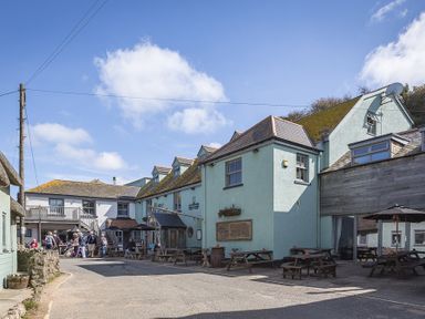 An outdoor seating area with picnic tables and umbrellas outside buildings at 4 Armada House in Hope Cove