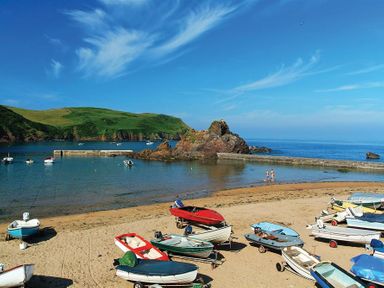 A beach with small boats on the sand and water a rocky outcrop and green hills at 4 Armada House in Hope Cove