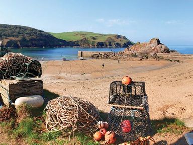 A sandy beach with fishing nets ropes and lobster pots by the shore at 4 Armada House in Hope Cove