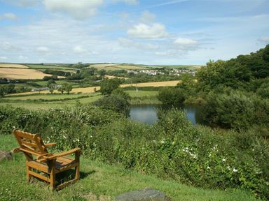 A wooden bench overlooking a pond with fields and trees in the background at Cowslip Cottage in Frogmore