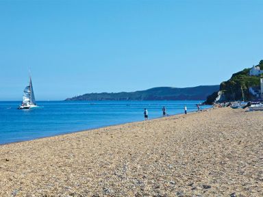 A beach with people fishing near the shore and a sailboat in the water at Cowslip Cottage in Frogmore