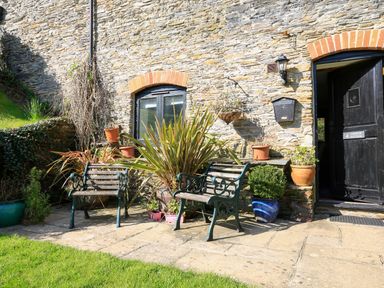 A stone wall with two benches and potted plants near a black door at Cowslip Cottage in Frogmore