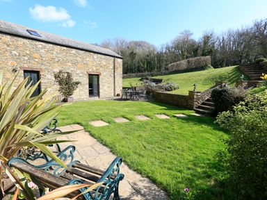 A stone building with a black door and window beside a grassy garden with chairs and a table at Cowslip Cottage in Frogmore