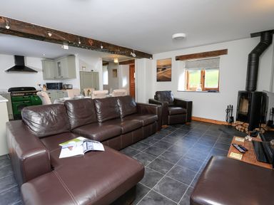 A living room with brown leather sofas a wood stove and an open kitchen at Cowslip Cottage in Frogmore