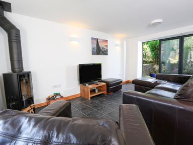 A living room with leather sofas a wood burner television and glass doors leading to a garden at Cowslip Cottage in Frogmore