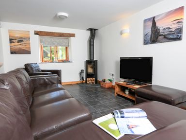 A living room with brown leather sofas a wood burning stove a television and pictures of seascapes on the walls at Cowslip Cottage in Frogmore