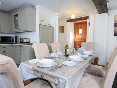 A dining table set with white dishes glasses and cutlery in a kitchen with green cabinets and a wooden door at Cowslip Cottage in Frogmore
