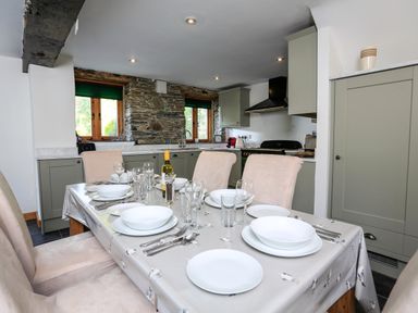 A dining table set with plates glasses and cutlery in a kitchen with green cabinets and stone wall at Cowslip Cottage in Frogmore