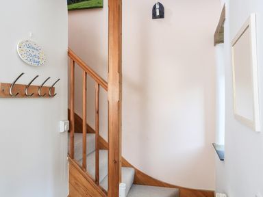 A wooden staircase with beige carpet next to a wall with coat hooks and a welcome sign at Cowslip Cottage in Frogmore