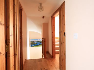 A hallway with wooden floors wooden door frames a light switch and stairs in Cowslip Cottage in Frogmore